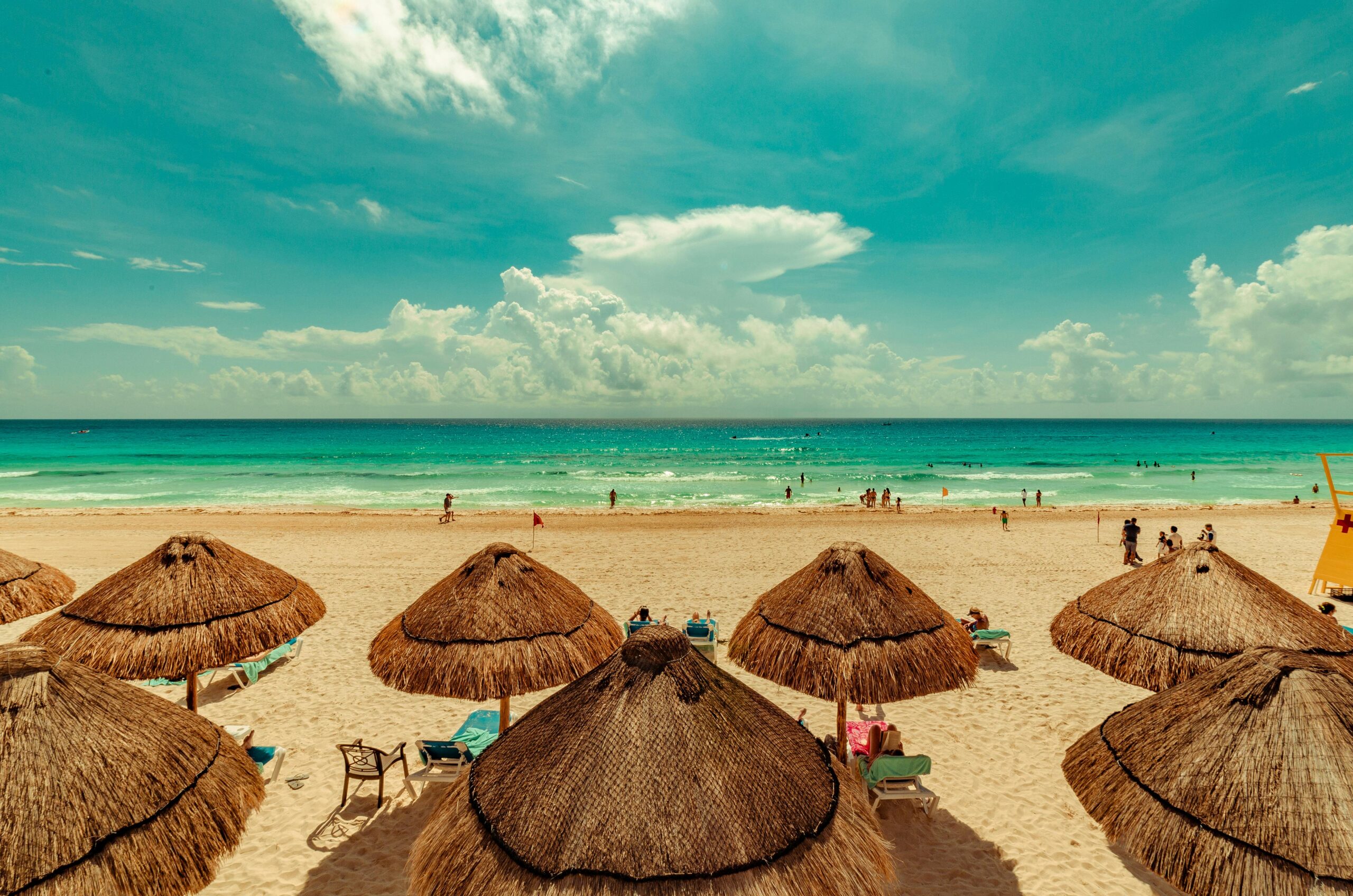 pexels-photo-2598663-2598663 A vibrant beach scene in Cancun, Mexico with straw umbrellas and turquoise sea under a bright sky.